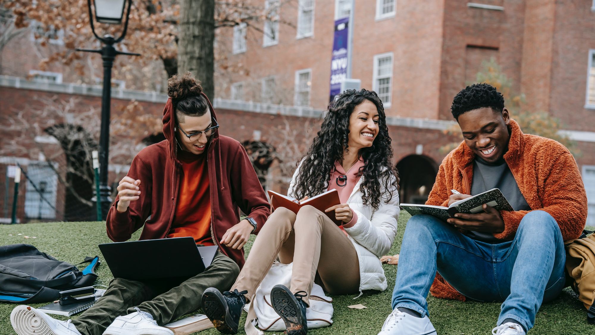 Students sitting together on a campus lawn, talking and working.